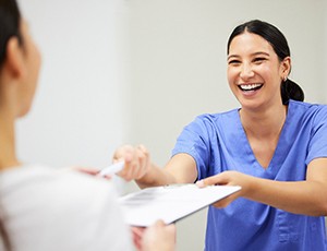 Smiling dental assistant handing patient forms