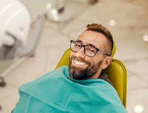 Man with glasses smiling while sitting in treatment chair