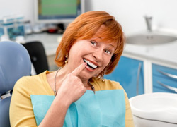 Woman sitting in the patient’s chair and pointing at her teeth